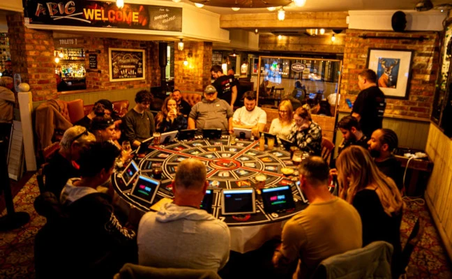 16 players sitting at a round table enjoying a game of Conspiracy