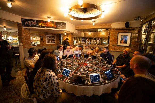 16 players sitting at a round table enjoying a game of Conspiracy